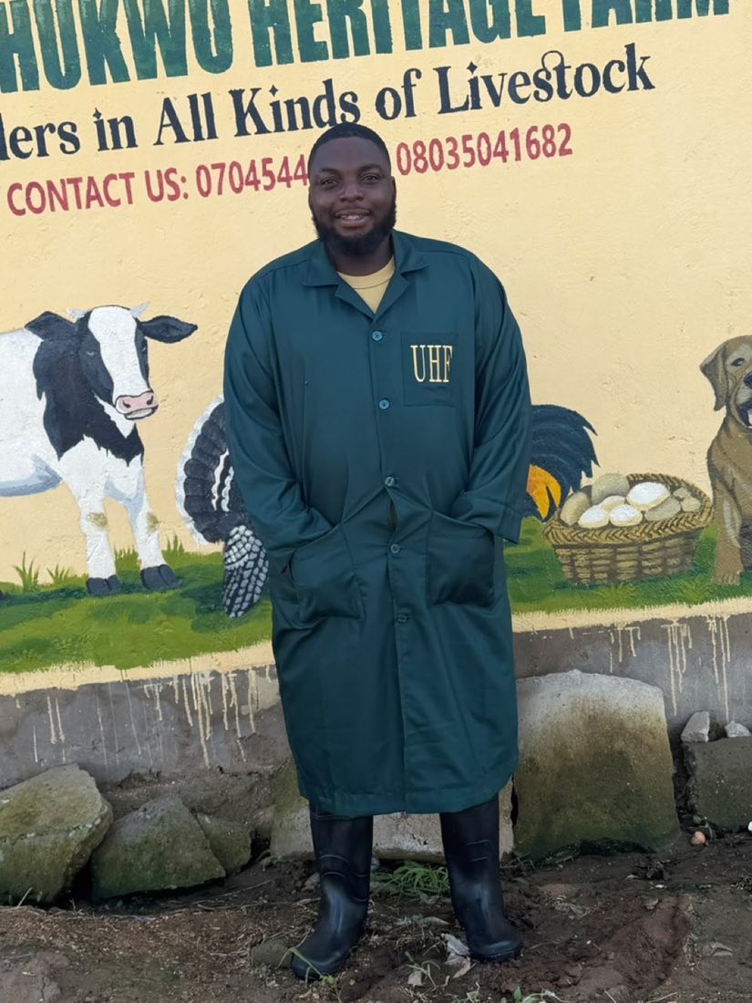 A farm manager in branded coveralls in front of the farm signboard